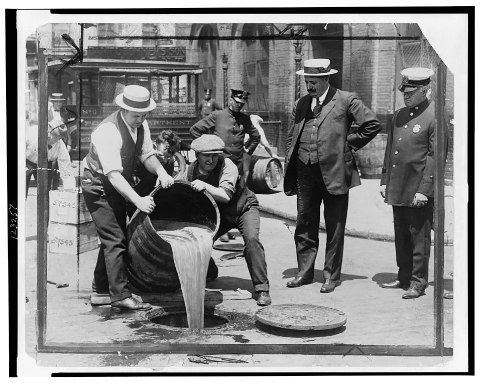 Prohibition agents pouring confiscated liquor into a street sewer while a police commissioner looks on